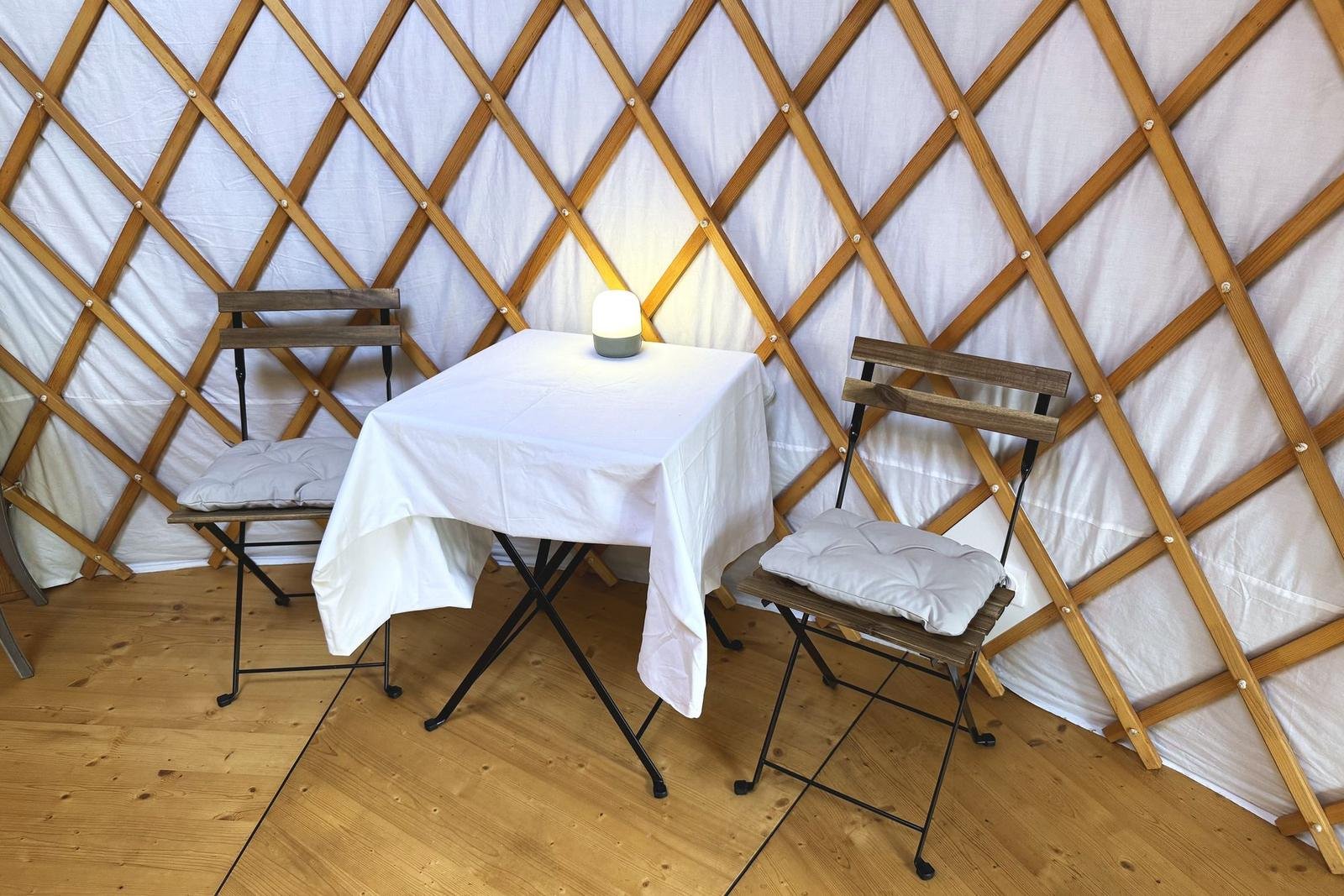 Petite table nappée, deux chaises et une lampe dans la yourte